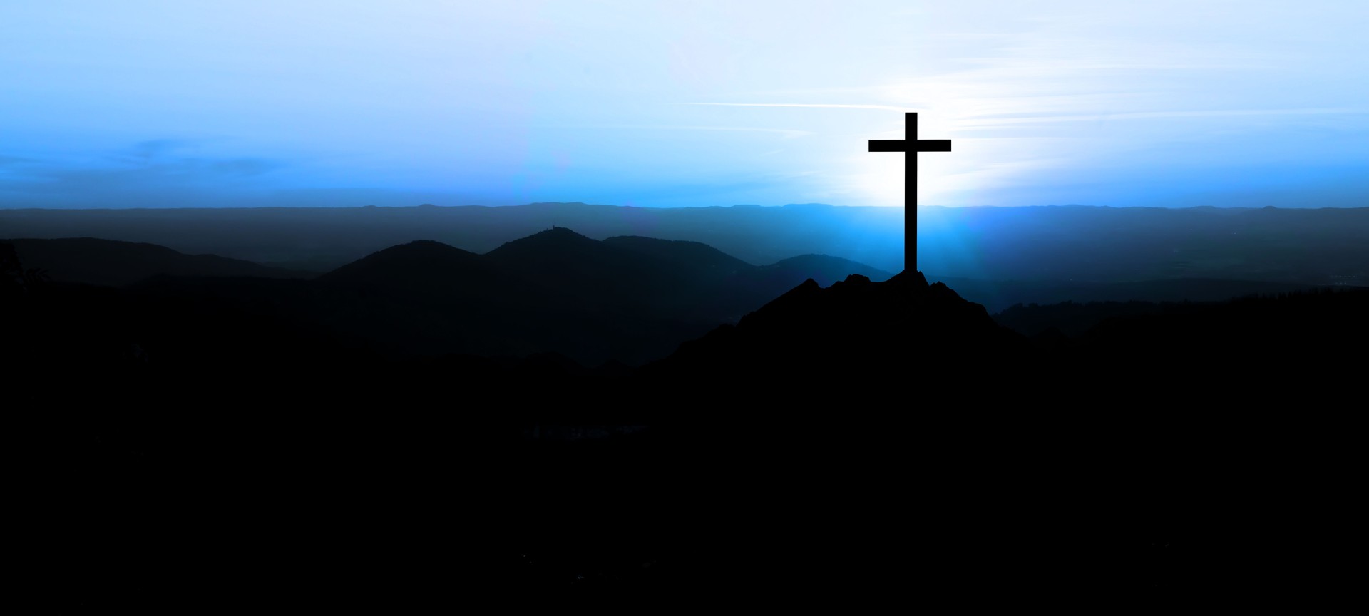 Religious grief landscape background banner panorama - Breathtaking view with black silhouette of mountains, hills, forest and cross / summit cross, in the evening during the sunset, with blue colored sky
